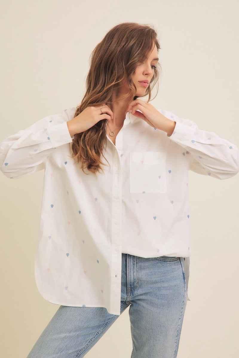Woman wearing a white button-up shirt with small blue heart patterns and light blue jeans