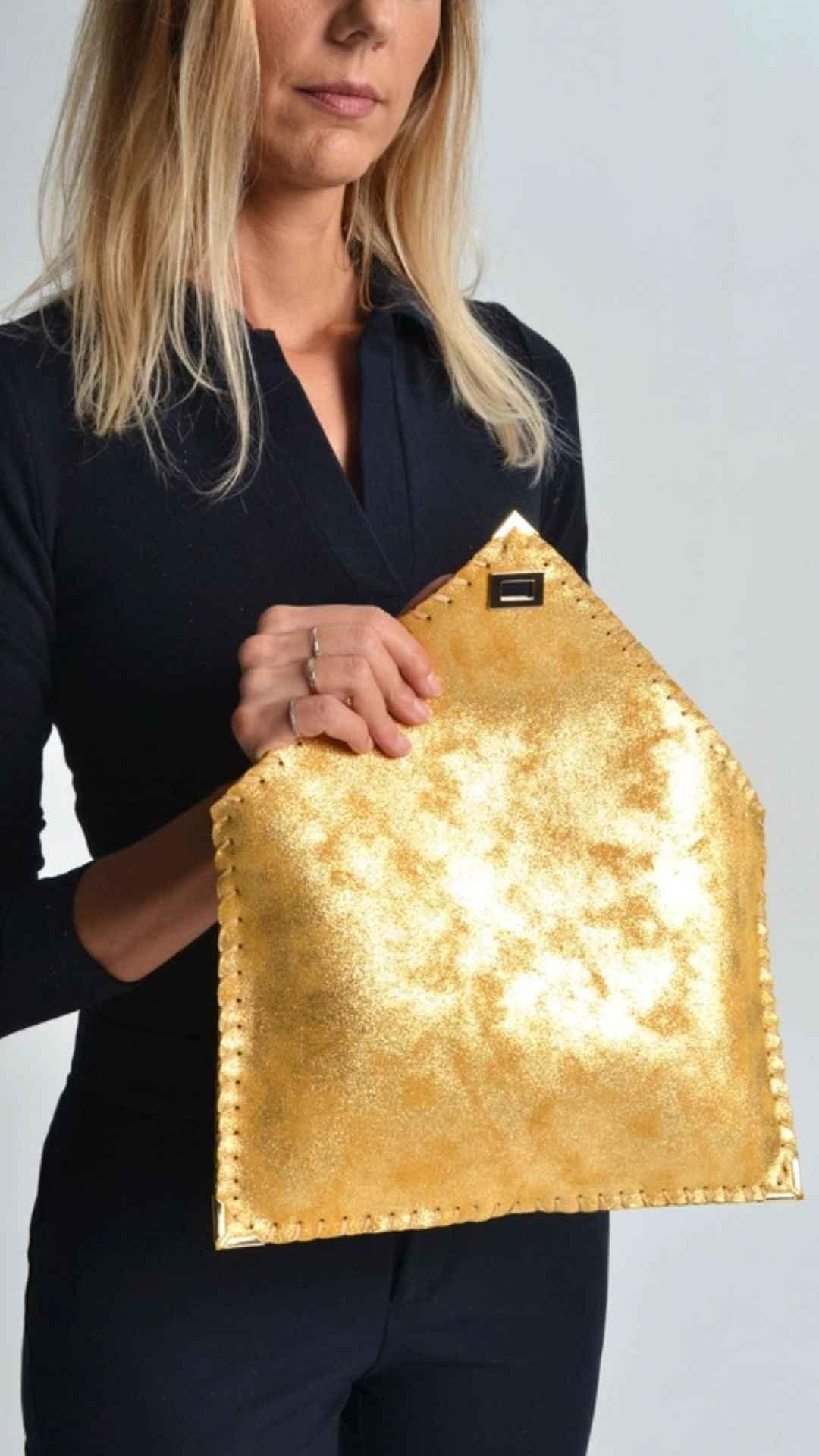 Woman holding a shiny gold envelope clutch bag, stylish accessory from Love Classic