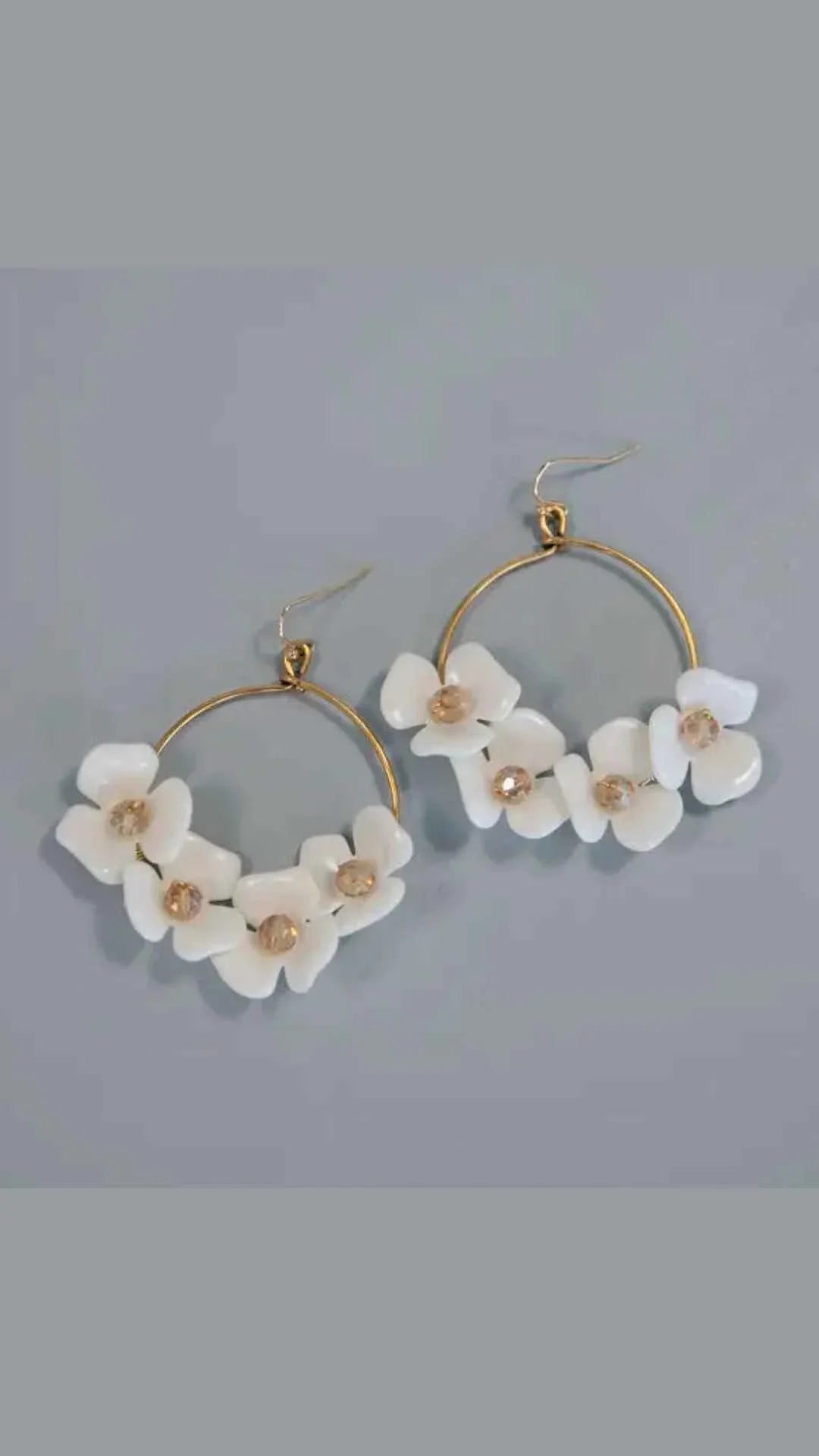 Gold hoop earrings with white floral accents and crystal centers on gray background