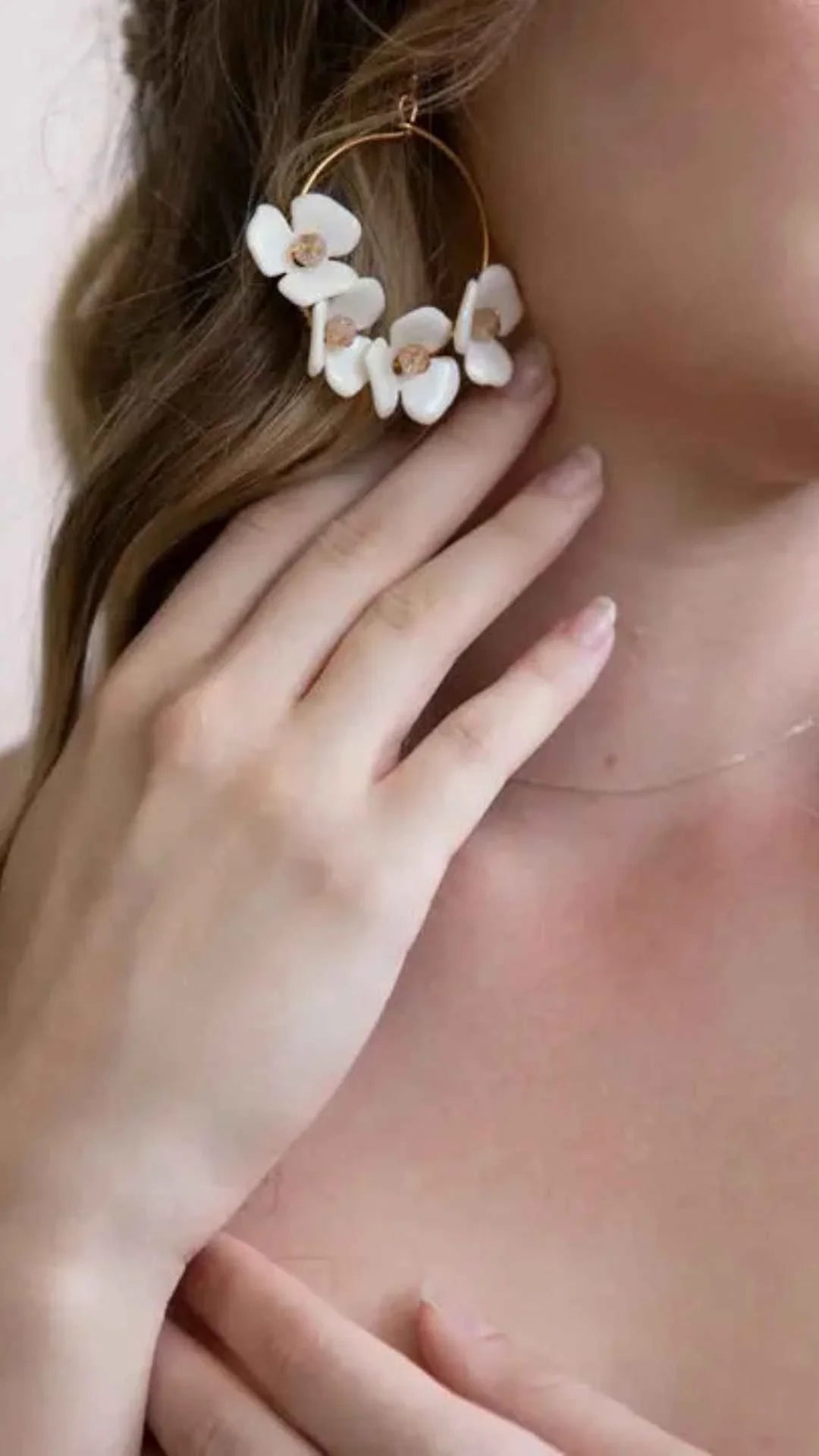 Woman wearing large gold hoop earring with white floral accents, Love Classic jewelry style