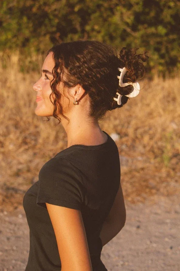 Woman with curly hair in a black top and claw clip, outdoors in golden sunlight
