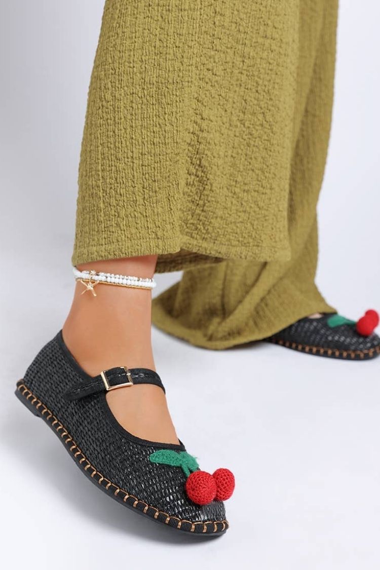 Cherry Accent Mary Jane Flats, black woven Mary Jane flats with cherry detail and buckle strap, paired with a textured olive-green dress and minimal anklet, showcasing a relaxed yet playful daytime look.