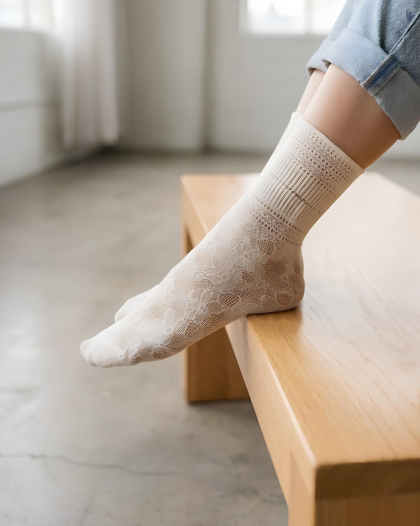 Sheer Floral Lace Crew Socks in ivory with intricate lace floral pattern, worn with rolled cuff jeans while resting on a wooden bench indoors, highlighting the delicate texture and lightweight feel.