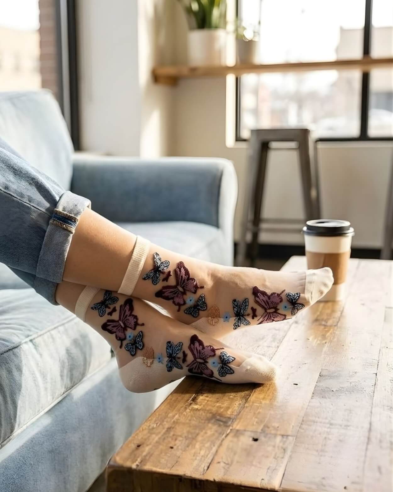 Butterfly Sheer Socks 2-Pack featuring lightweight sheer material with colorful butterfly embroidery, styled in a cream tone while lounging on a sofa with a coffee table and window-lit background.