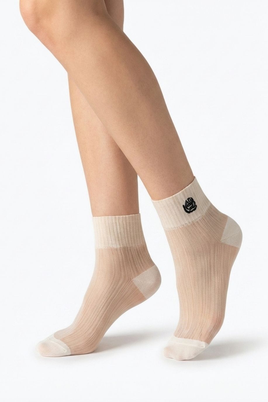 Close-up of cream sheer ribbed ankle socks with contrasting rose embroidery, shown on crossed feet against a plain white background to emphasize texture and transparency.