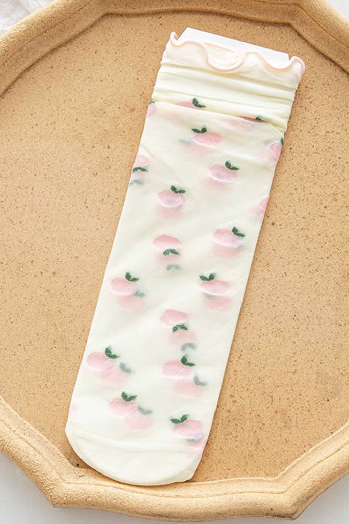 Sheer mesh crew socks with a pastel pink plums pattern and a soft lettuce-edge cuff on a neutral background.