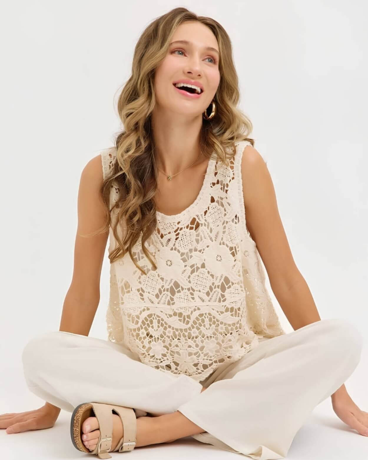 Crochet Lace Tank Top featuring a cream floral crochet lace design with scalloped hem, shown on a seated model paired with light wide-leg pants, relaxed studio view.