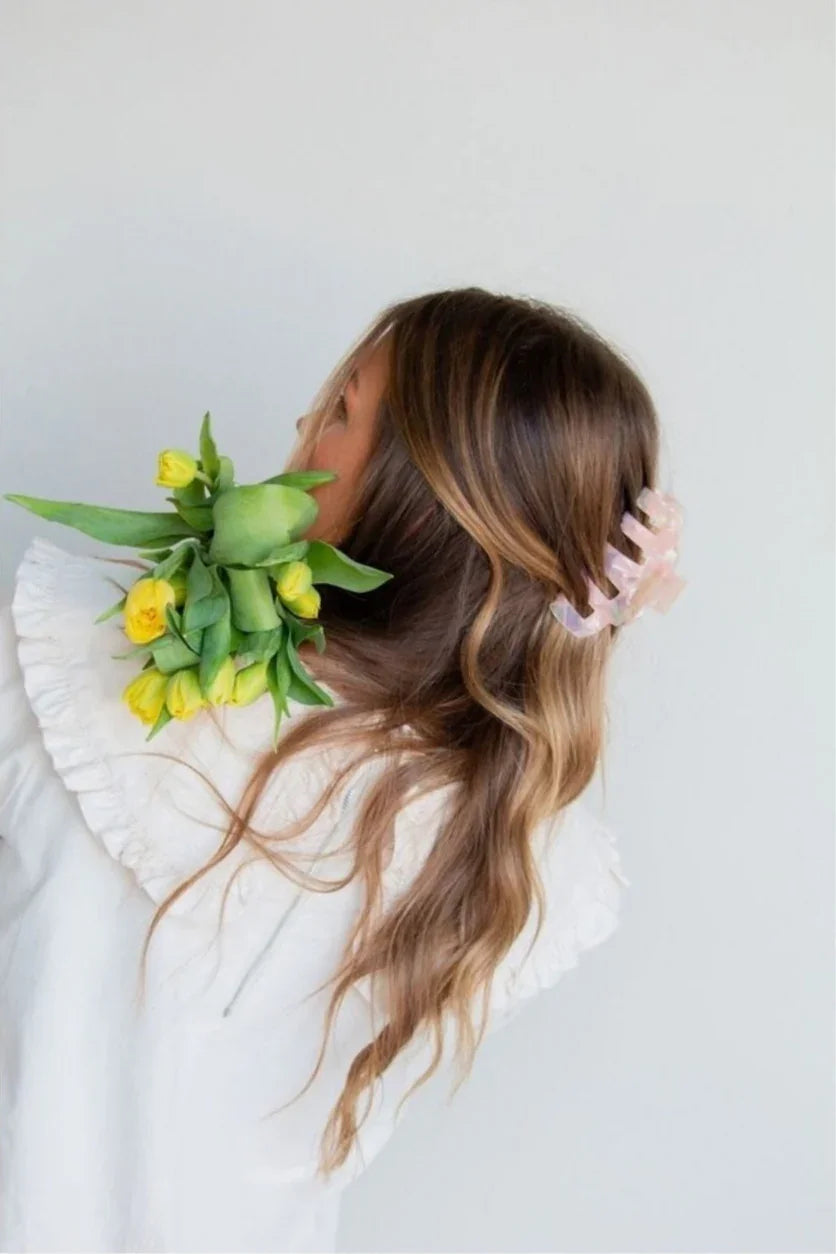 Woman wearing white ruffled blouse, holding yellow tulips, hair styled with pink claw clip