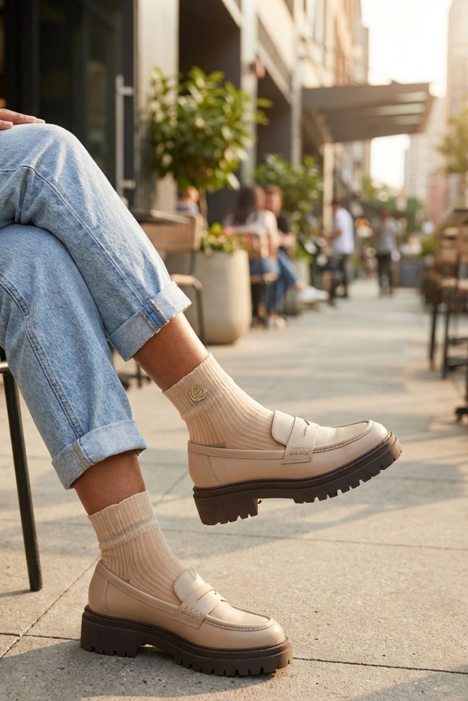 Beige sheer ribbed ankle socks with rose embroidery worn with chunky loafers and rolled jeans, styled outdoors on a city sidewalk café.
