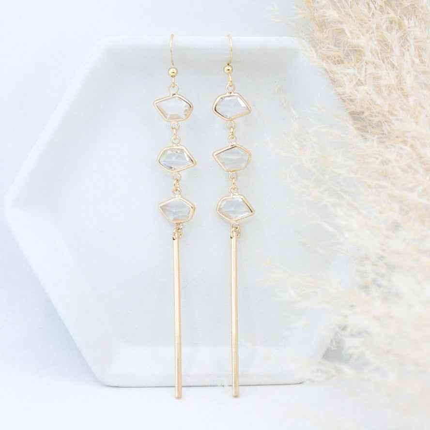 Elegant gold dangle earrings with geometric crystal accents on a white dish, Love Classic jewelry