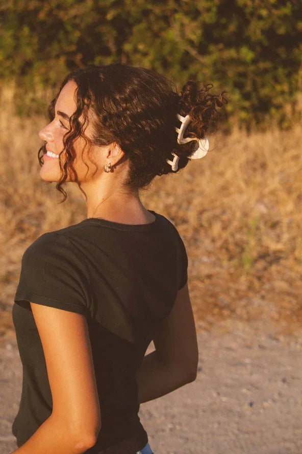 Woman with curly hair and white claw clip outdoors, wearing black top, Love Classic style