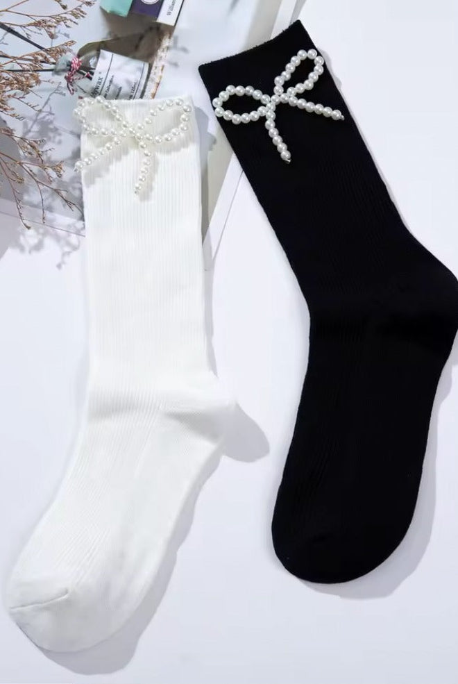 Black and white ribbed crew socks featuring delicate pearl bow embellishments, styled flat lay on a light background.