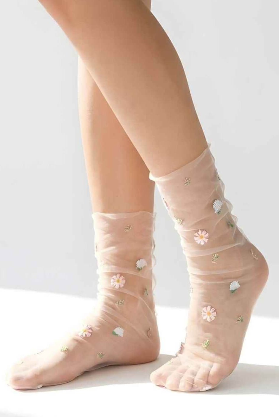 Sheer Garden Daisy Crew Socks in blush nude mesh with embroidered daisy flowers, shown on crossed legs against a clean light background to highlight the transparent fabric.