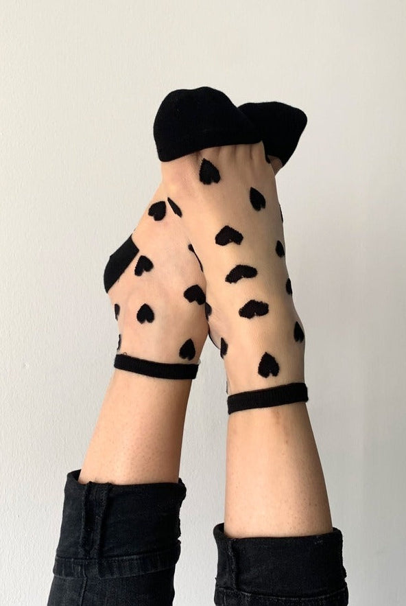 Sheer socks with black heart patterns, modeled with black pants, Love Classic style