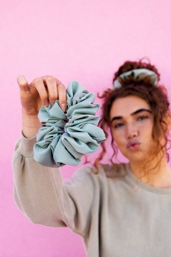 Model styled with the Eucalyptus Jumbo Scrunchie on a pink background highlighting the jumbo silhouette and smooth matte sateen texture.