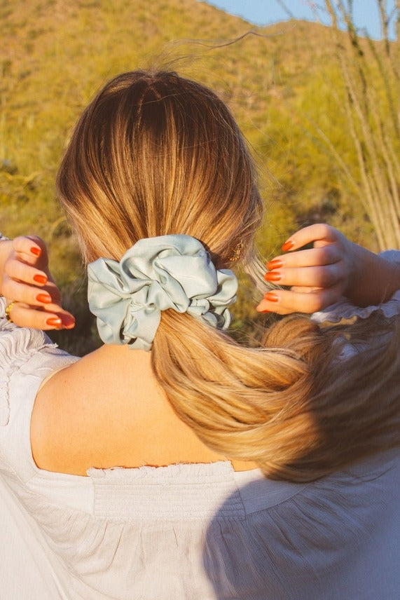 Back view of model wearing the Eucalyptus Jumbo Scrunchie in light blue green sateen fabric styled around a ponytail with oversized gathered volume.