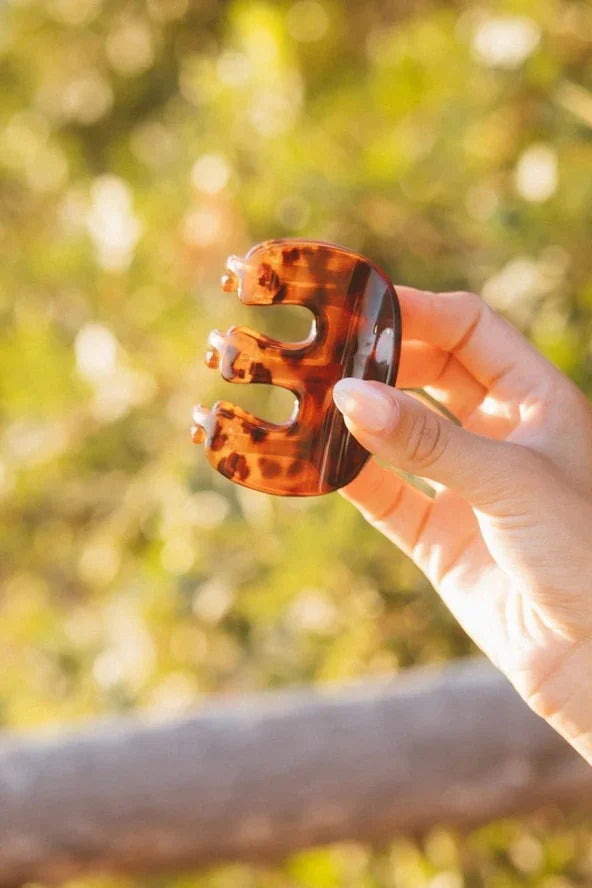 Hand holding brown tortoise shell hair claw clip outdoors, Love Classic accessory