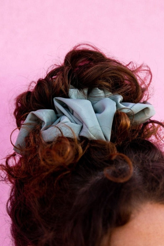 Close-up of the Eucalyptus Jumbo Scrunchie on a pink background showing the luxe sateen fabric and light blue green matte finish.