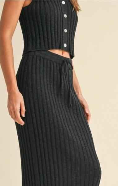 Woman wearing ribbed black knit two-piece set with sleeveless top and drawstring skirt