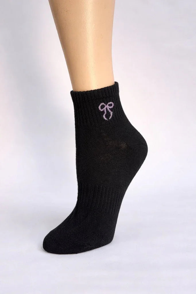 Black ankle sock with purple bow embroidery on mannequin foot, minimalist background