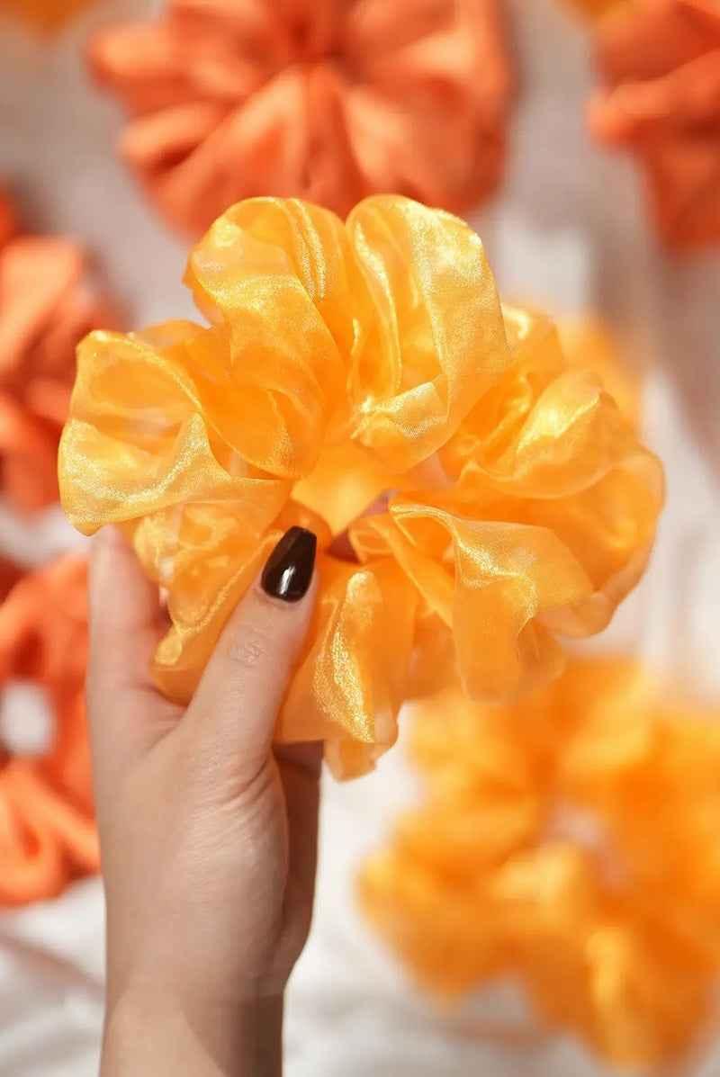Hand holding golden satin scrunchie by Love Classic, vibrant hair accessory on display