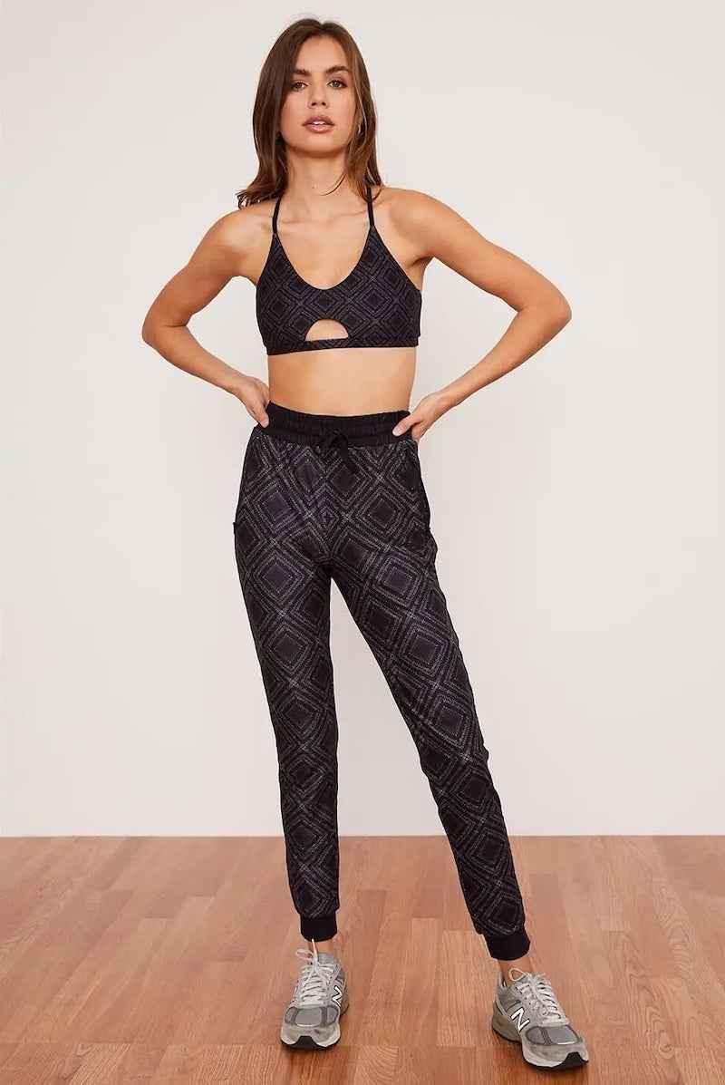 Woman modeling Love Classic black patterned joggers and sports bra set on wood floor
