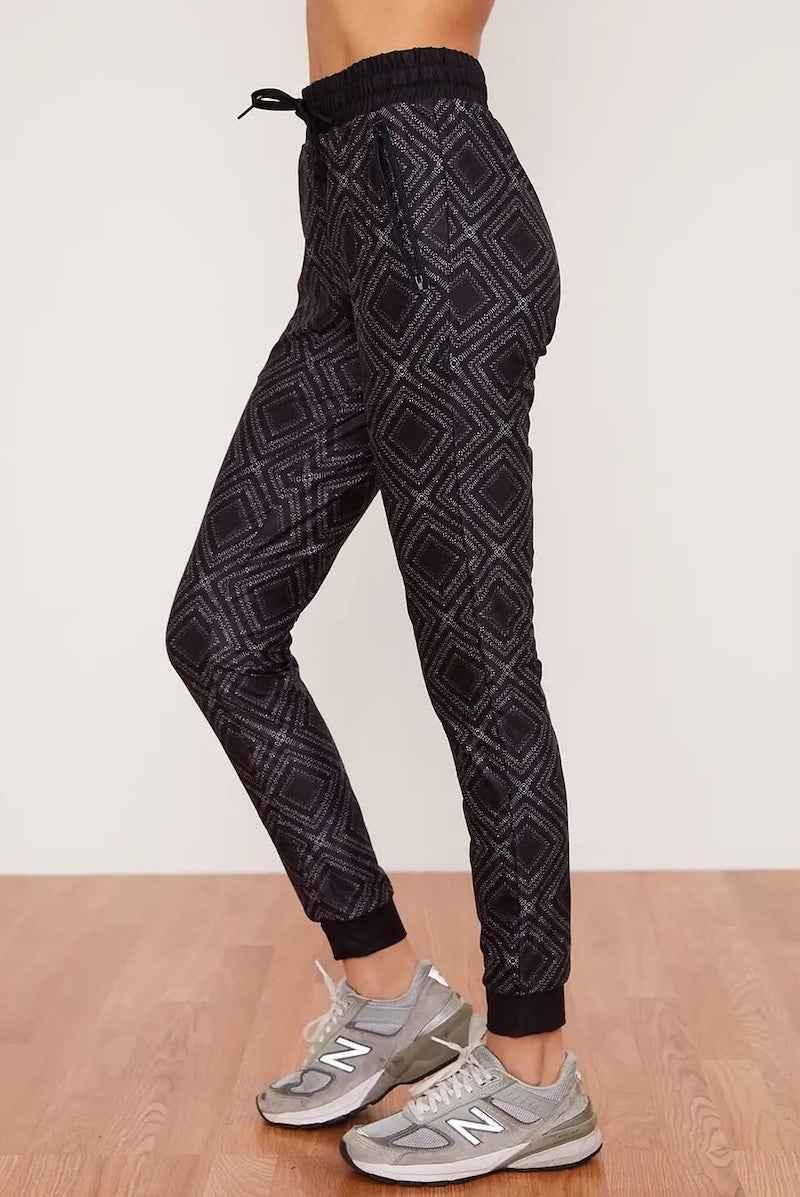 Love Classic geometric print jogger pants with drawstring waist and gray sneakers on wood floor