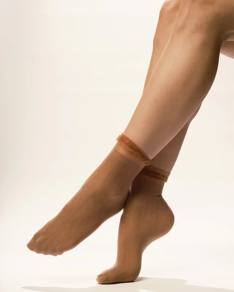 Sheer nude ankle socks on crossed legs with neutral background