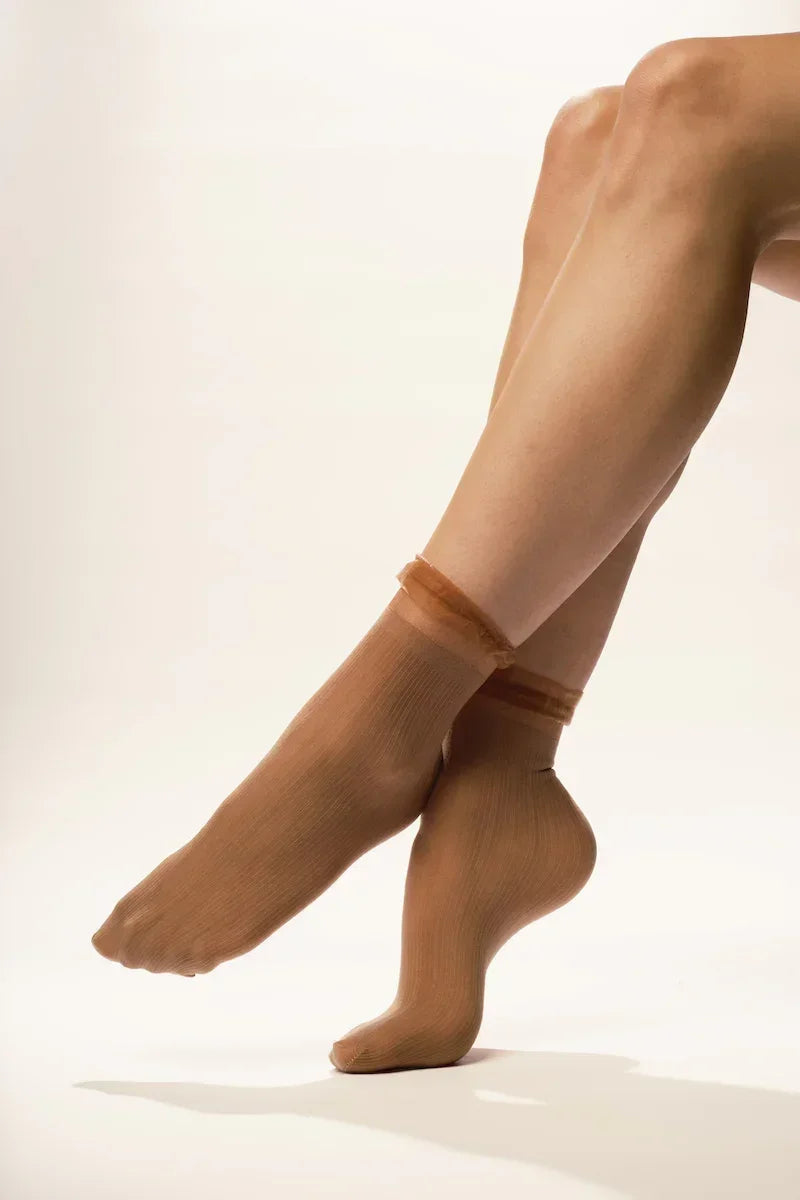 Sheer nude ankle socks on crossed legs with neutral background