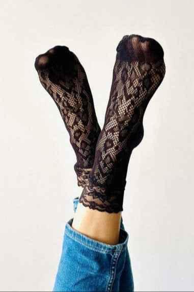 Woman wearing black lace socks with floral pattern, legs raised, blue jeans, Love Classic style.
