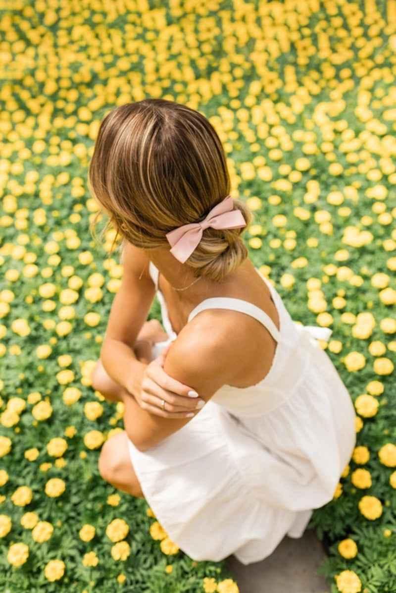 Woman in white dress with pink hair bow sitting in field of yellow flowers, Love Classic style