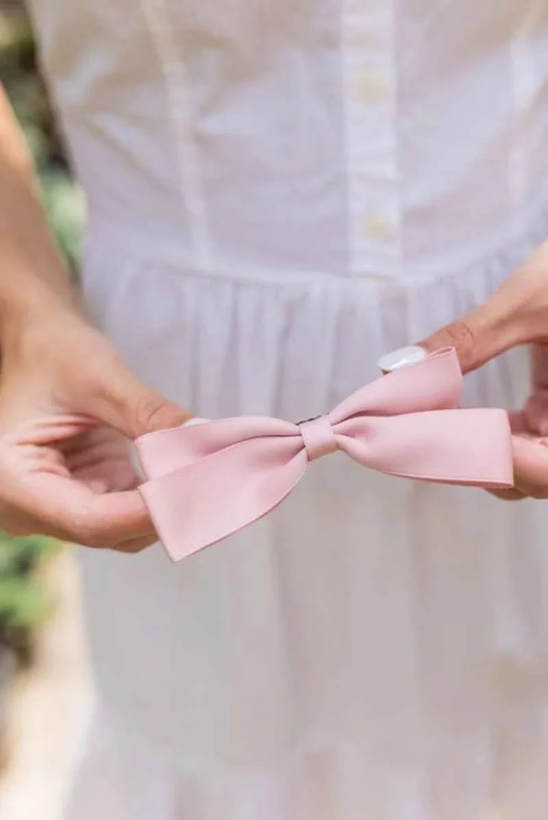 Woman holding a pink bow accessory in front of a white dress, Love Classic style