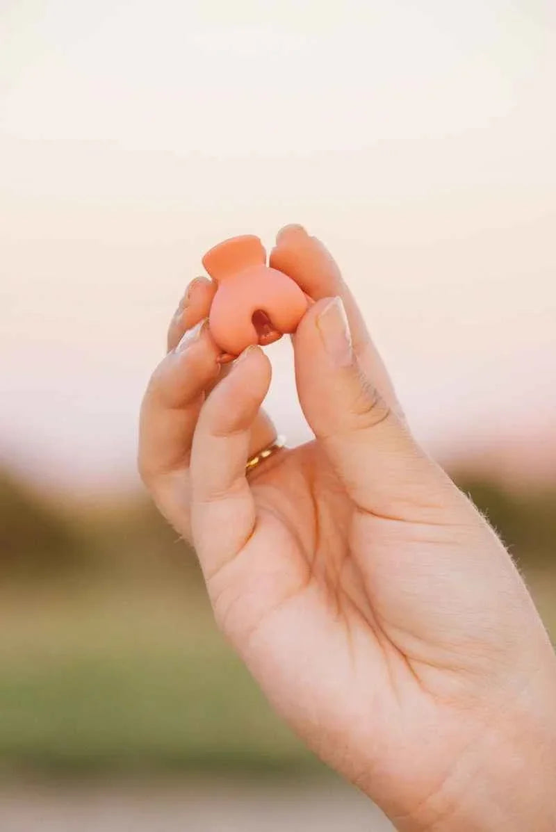 Hand holding a small terracotta-colored ceramic vase outdoors, Love Classic style