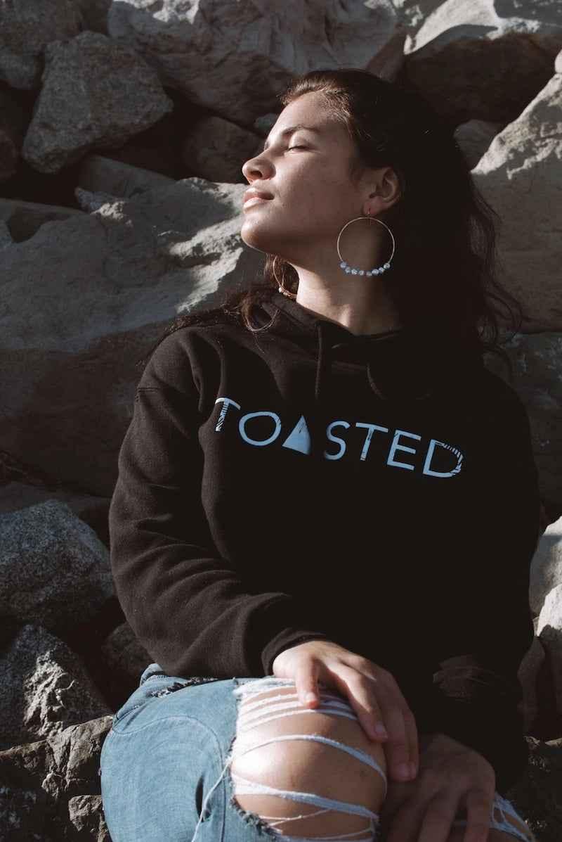 Woman in black Toasted sweatshirt and hoop earrings outdoors on rocks, Love Classic style