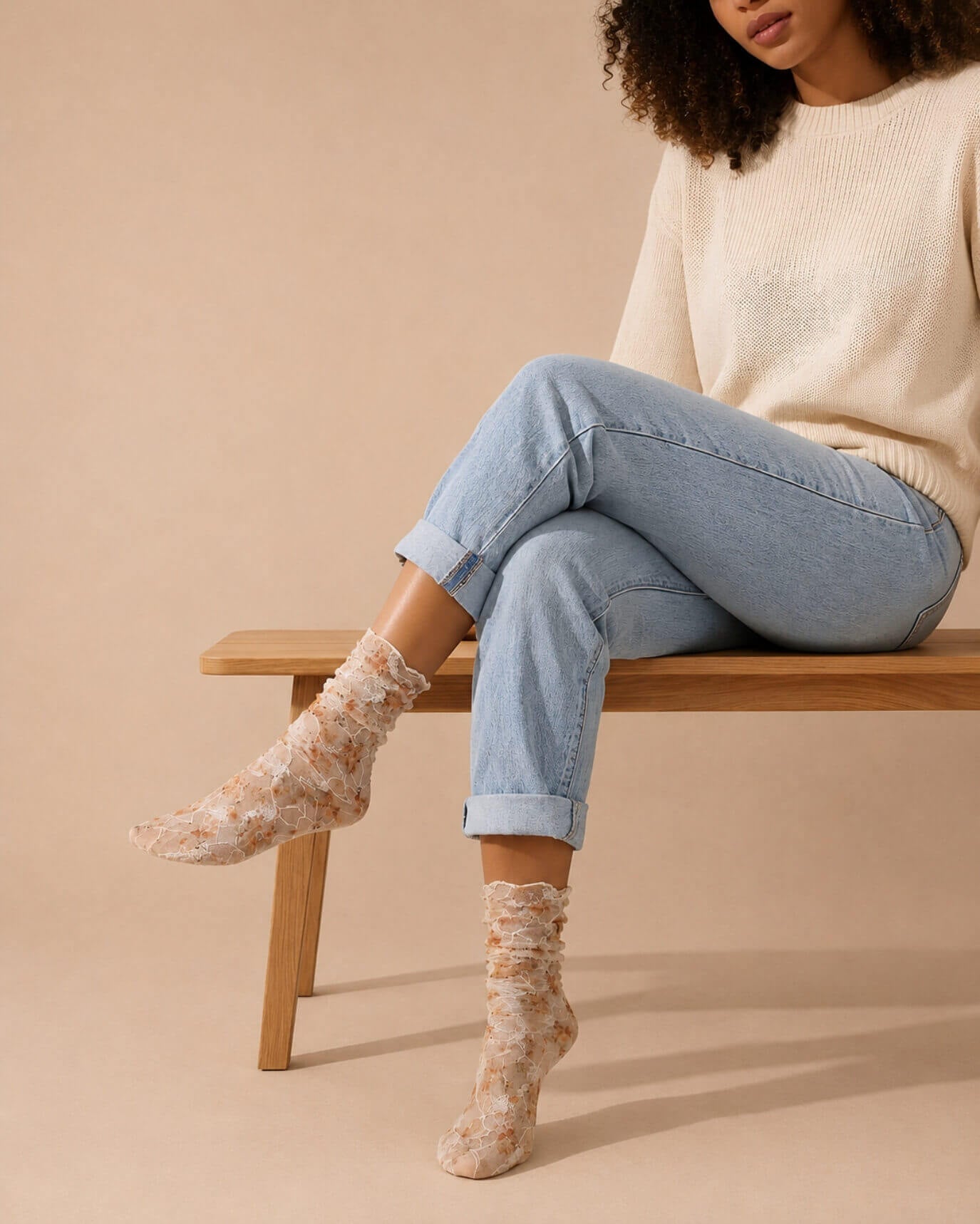 Floral mesh sheer socks in orange with delicate lace overlay and soft floral print, styled with rolled cuff jeans and a knit sweater while seated on a wooden bench, highlighting the lightweight, semi-transparent fabric and feminine design.