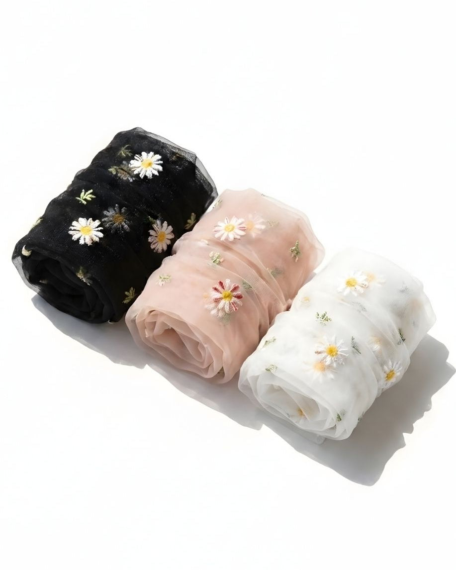 3-pack sheer garden daisy crew socks in black, blush pink, and white, rolled together on a clean white surface to highlight the delicate sheer fabric and embroidered daisy details.