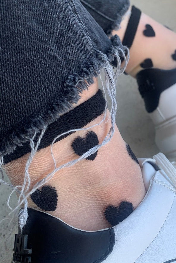 Sheer socks with black heart patterns, frayed black jeans, and white sneakers by Love Classic