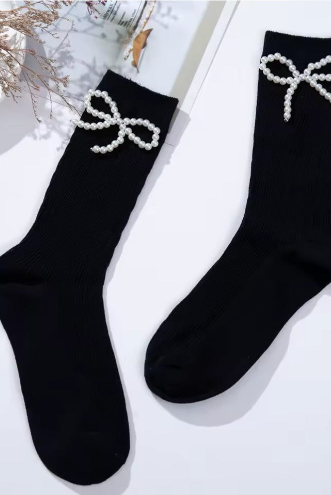 Black ribbed crew socks featuring delicate pearl bow embellishments, styled flat lay on a light background.