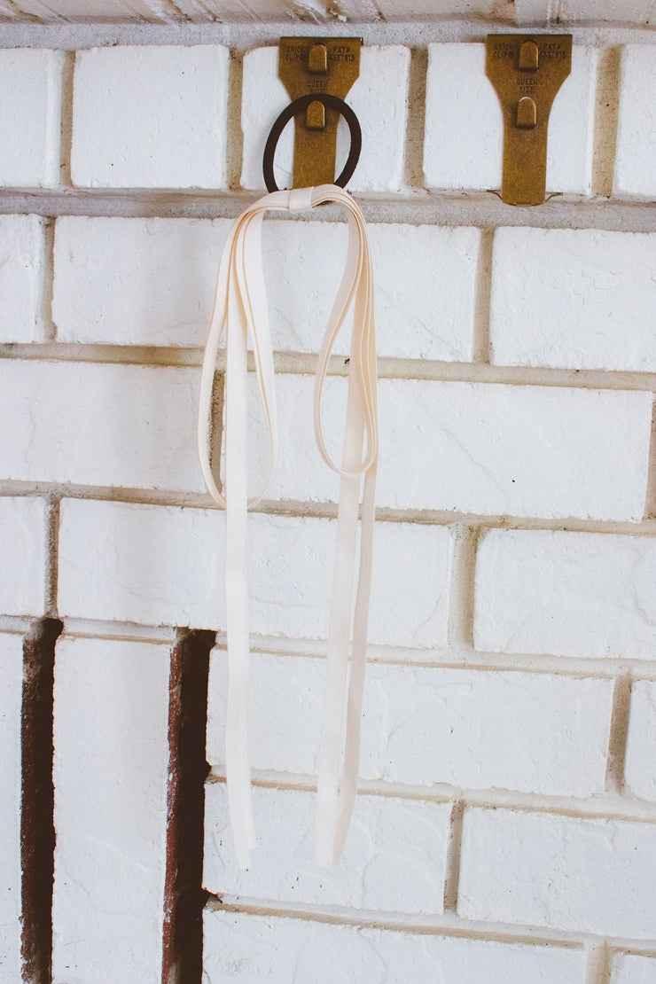 Light pink ribbons and a black hair tie hanging on a metal hook on a white brick wall