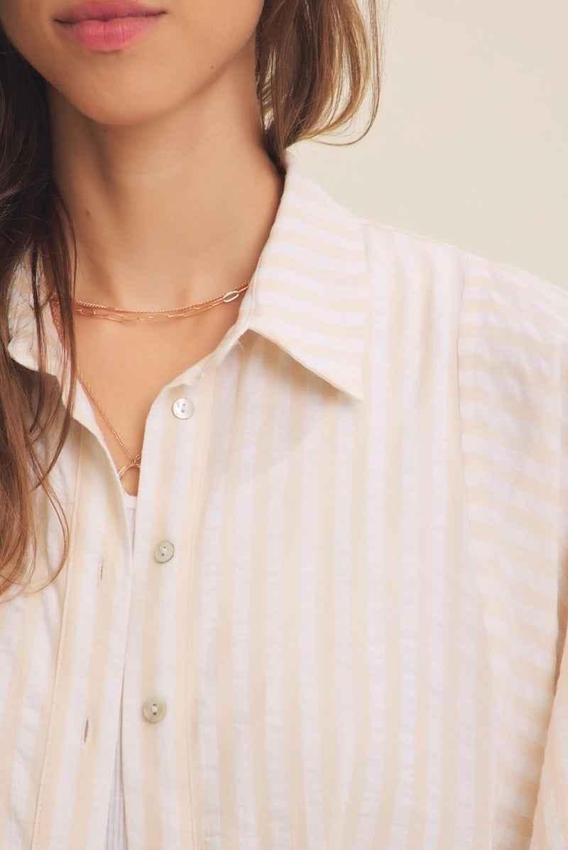 Woman wearing a beige striped button-up shirt and delicate gold necklace, Love Classic style