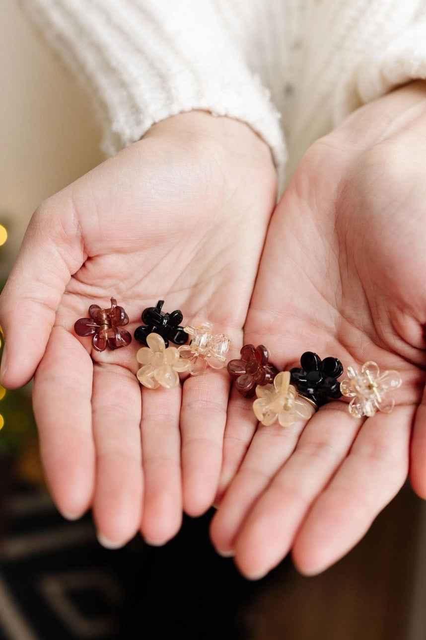 Hands holding assorted flower-shaped hair clips in neutral and black colors, Love Classic accessories