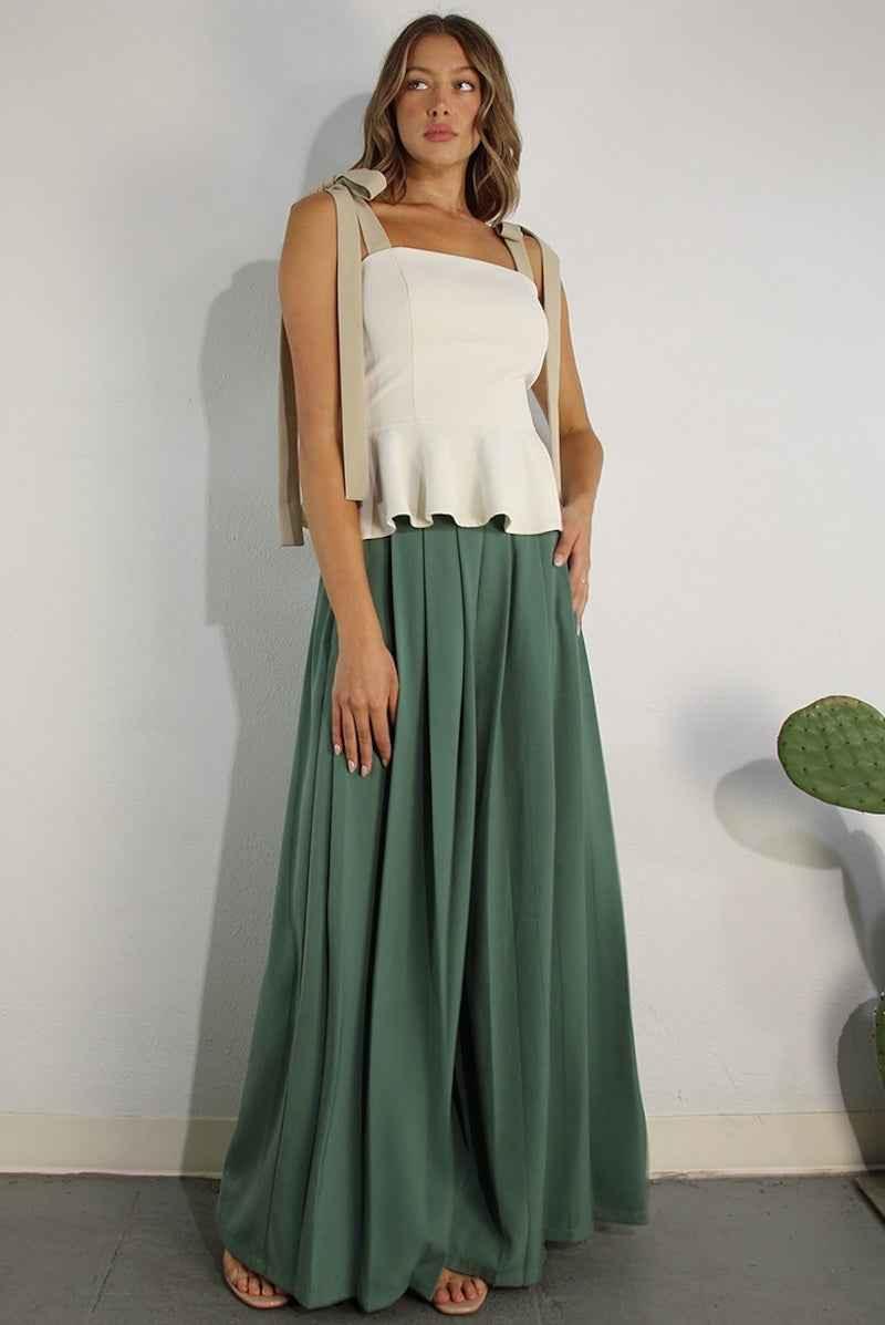Woman modeling a chic cream peplum top with tie straps and flowy green maxi skirt from Love Classic