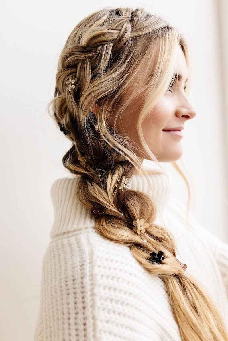Woman with blonde braided hair styled with flower clips, wearing a white knit sweater