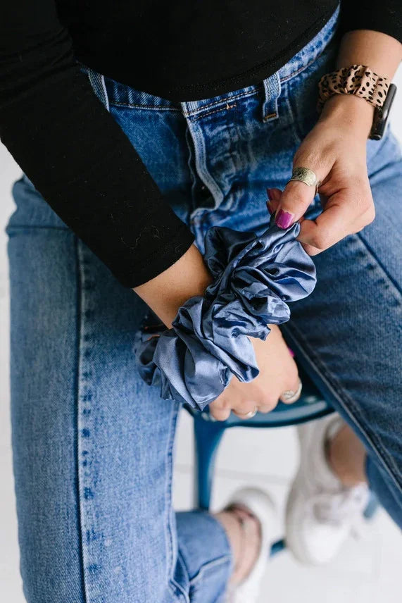 Woman in jeans and black top wearing a blue satin scrunchie from Love Classic