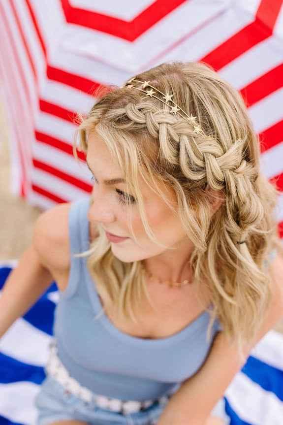 Woman with braided blonde hair and star headband on beach, under red and white umbrella, Love Classic style