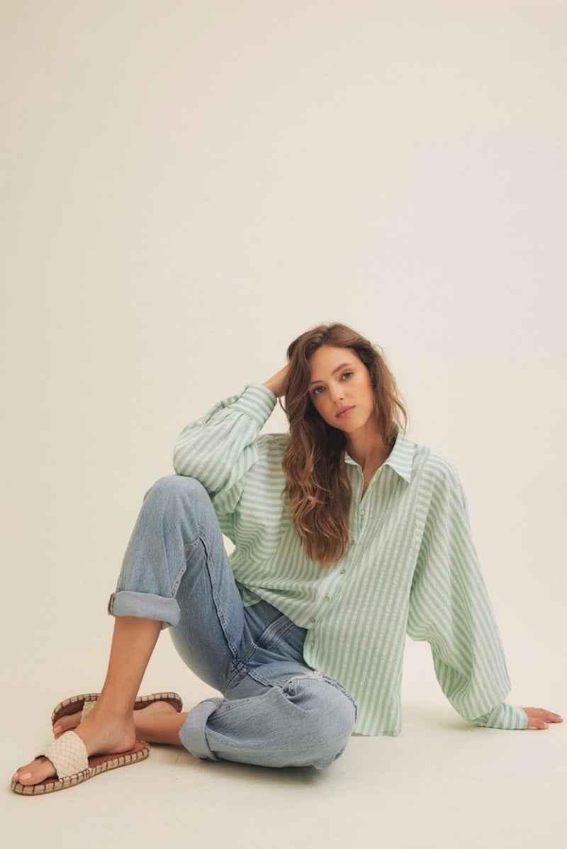 Woman in mint green striped shirt and jeans from Love Classic, sitting on light background