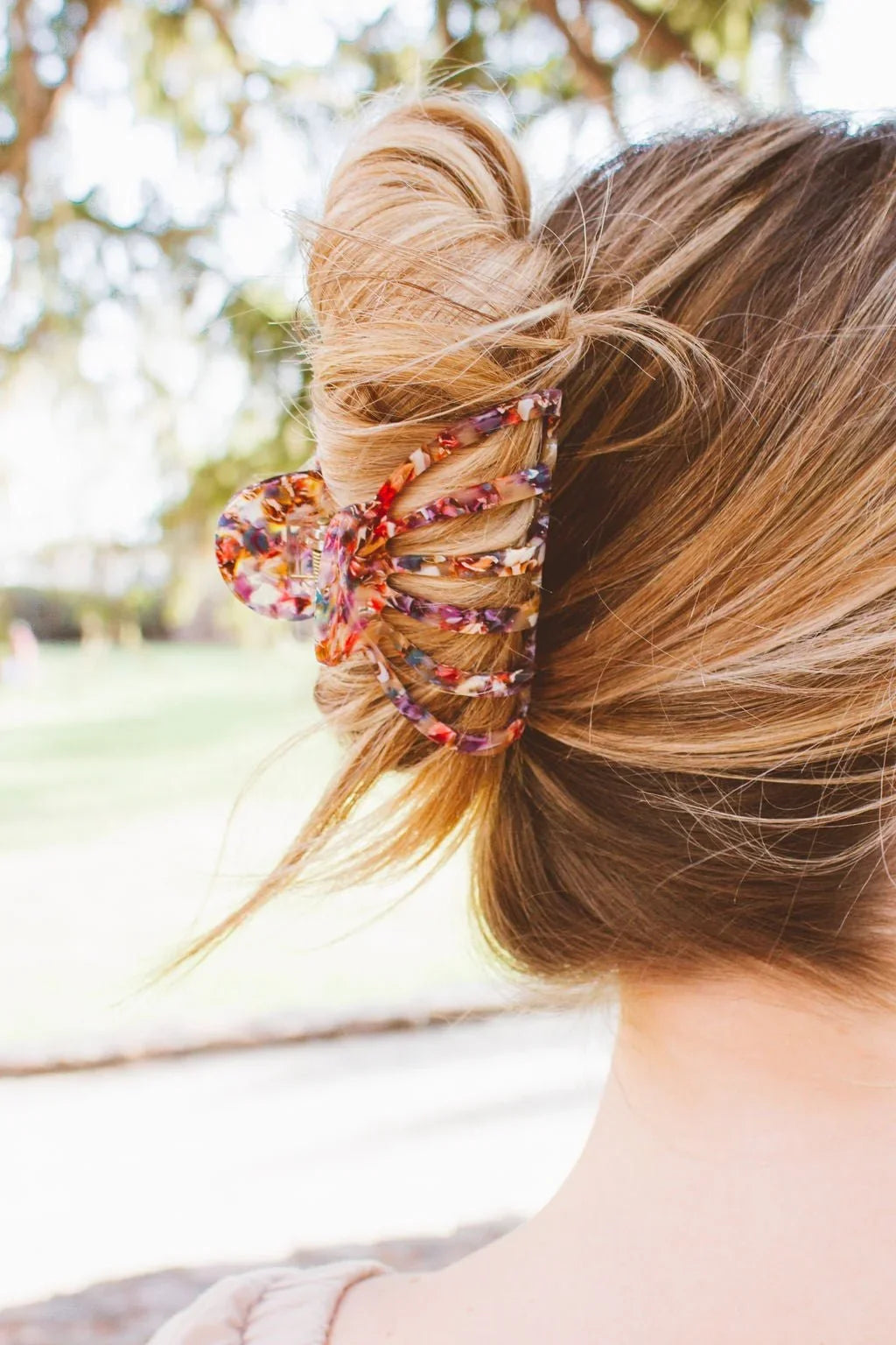 Woman wearing a colorful floral claw clip in blonde hair, outdoor park setting, Love Classic