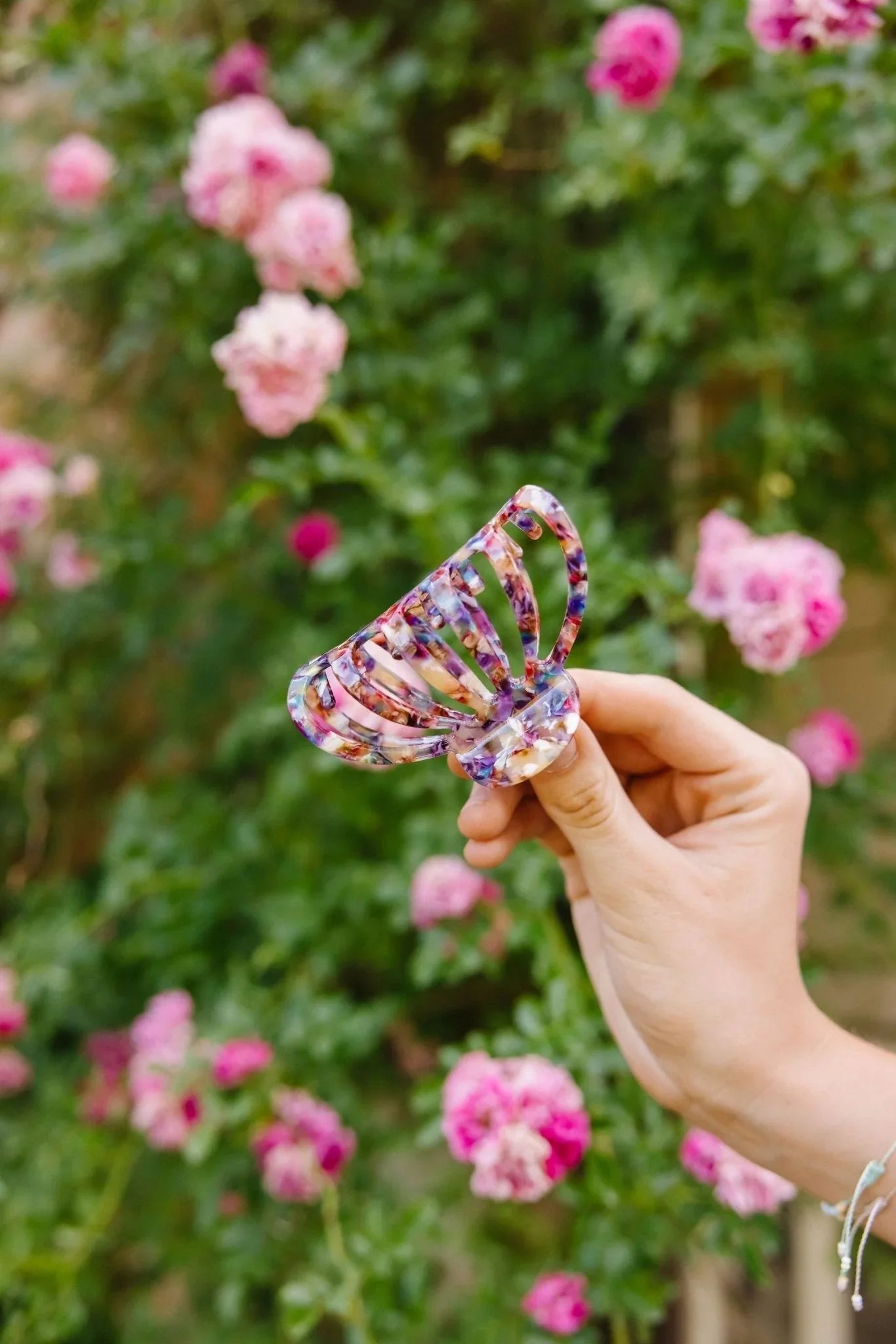 Hand holding colorful tortoiseshell claw hair clip from Love Classic in garden with pink roses