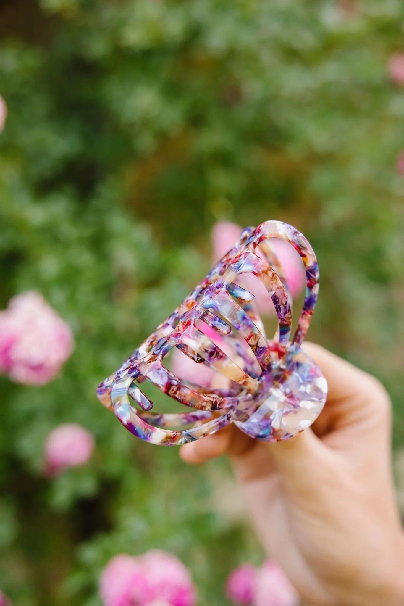 Colorful acetate claw clip held outdoors near pink flowers, Love Classic hair accessory