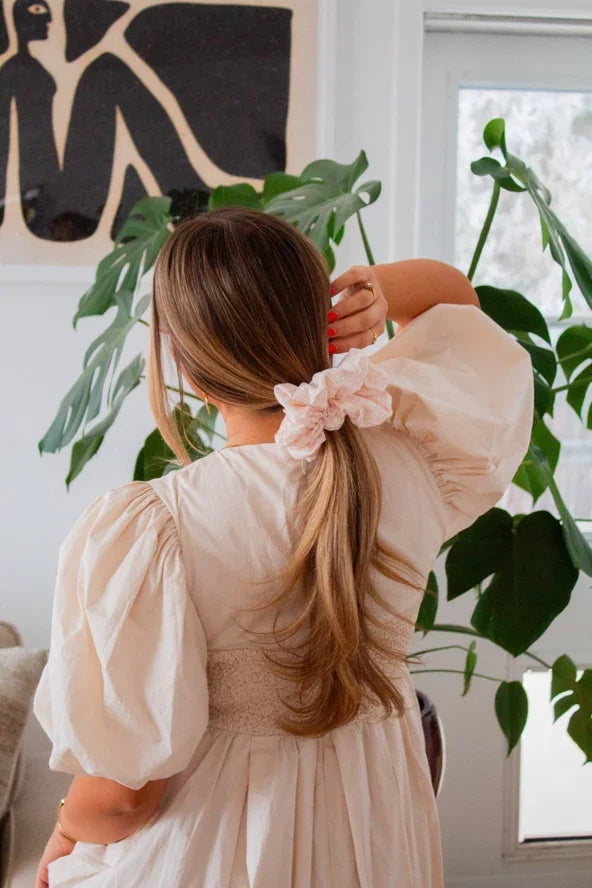 Woman in cream puff sleeve dress with pink scrunchie, Love Classic style, indoor setting